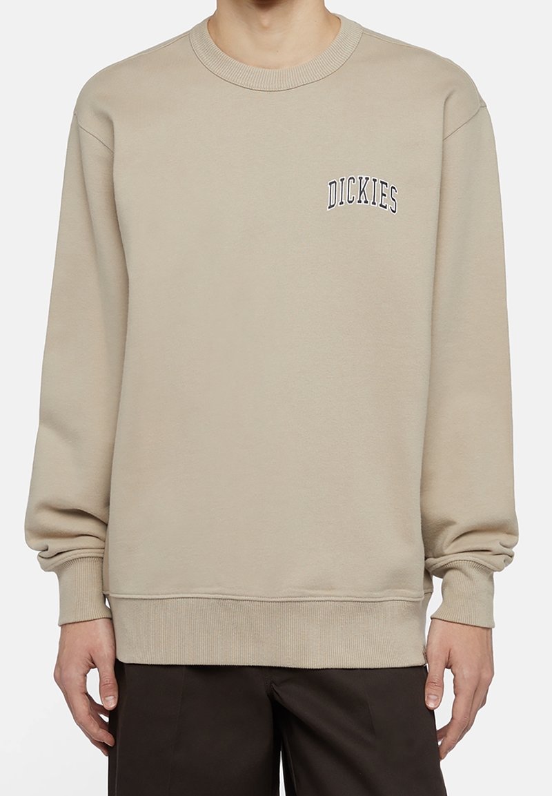 Felpa girocollo beige realizzata in misto cotone con polsini e orlo a costine. Sul davanti è presente il logo "DICKIES" in ricamo blu scuro.