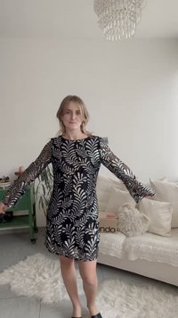 Vestido preto com mangas compridas e transparentes com padrões de folhas prateadas, corpete justo, bainha em folho e tecido liso.