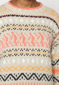 Maglione lavorato a maglia con una base color crema, caratterizzato da motivi multicolori in arancione, nero e bianco. Collo a costine e tessuto testurizzato.