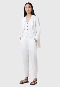 Completo bianco su misura composto da un blazer, un gilet con bottoni neri e pantaloni a sigaretta, abbinato a sandali neri con cinturini. Tessuto morbido.