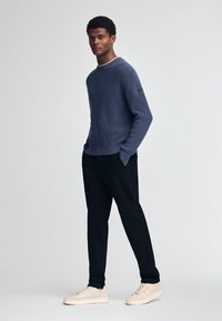 Marineblauwe geribbelde trui met ronde hals, zwarte slim-fit broek en lichtgekleurde sneakers, met een klein logo op de mouw van de trui.