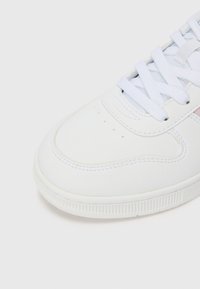 Hvit sneaker laget av glatt syntetisk materiale, perforert tå, hvite snører, lyseblå detaljer og en teksturert gummisåle.