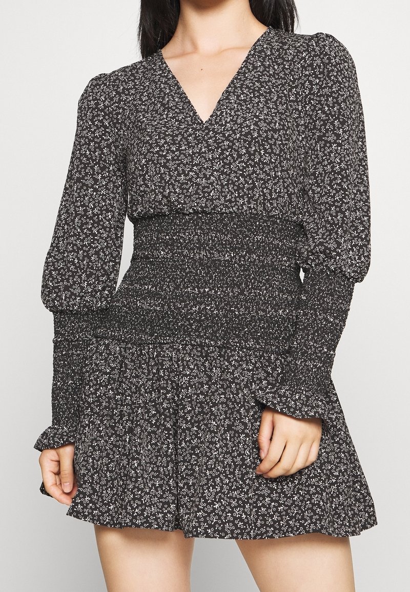 Černé šaty s bílým květinovým vzorem, s dlouhými nabíranými rukávy, výstřihem do V, smockovaným pasem a volným volánkovým lemem. Měkká textilie.