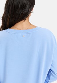 Sweat-shirt à col rond bleu clair avec une coupe décontractée, col côtelé et un petit accent métallique à l'arrière. Tissu doux, design minimal.