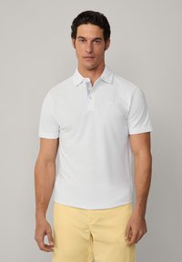 White polo shirt with a short collar, featuring a striped pattern on the inner collar. Made of a smooth fabric, paired with light yellow shorts.