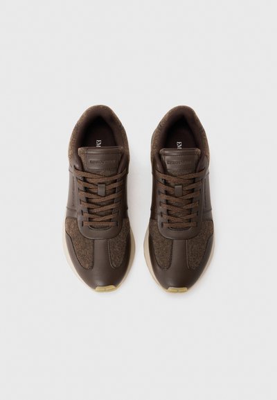 Braune Turnschuhe aus einer Kombination von glattem Leder und strukturiertem Stoff. Rundespitze, flache Schnürsenkel und hellfarbige Gummisohle.