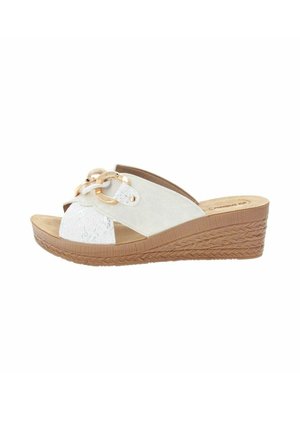 Sandale à talon compensé blanche avec semelle brune tressée texturée et anneaux décoratifs dorés sur de larges brides avant.