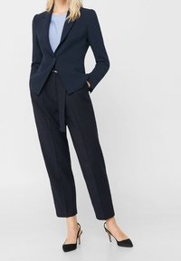 Blazer bleu marine à épaules structurées, coupe ajustée ; associé à un pantalon taille haute à rayures fines ; escarpins noirs à bout pointu ; haut bleu clair.