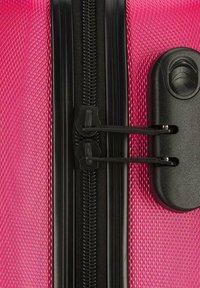 Pink textured suitcase with a black zipper. Features include dual zipper pulls and a black locking mechanism on the side.