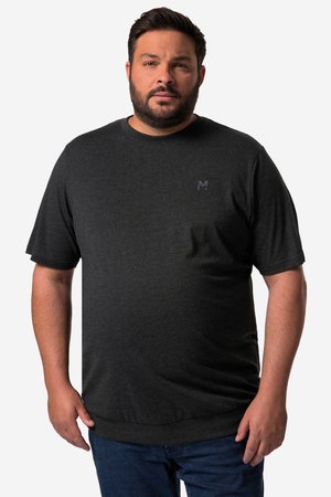 Mand med kort mørkt hår og skæg iført en mørkegrå t-shirt med korte ærmer og blå jeans, stående mod en ensfarvet baggrund.