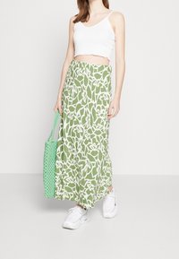 Falda maxi verde con patrón abstracto blanco, combinada con un top corto blanco y un bolso de textura verde menta, llevada con zapatillas blancas.