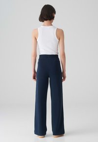 Marineblauwe wijde broek met een elastische tailleband en een achterzak, gecombineerd met een aansluitend wit tanktop, getoond vanuit de achterkant.