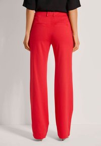Rote, weit geschnittene Hosen aus weichem Stoff mit glatter Textur. Mit einem Bündchen mit Gürtelschlaufen und zwei Gesäßtaschen.