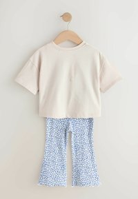 Világos bézs rövid ujjú crop top, kék virágos, bőszárú nadrággal, mely fehér virágmintákkal és hullámos szegéllyel rendelkezik.