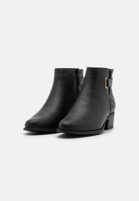 Botines negros de cuero liso con un tacón bajo en bloque, que presentan una cremallera lateral y un detalle acolchado en la parte trasera.