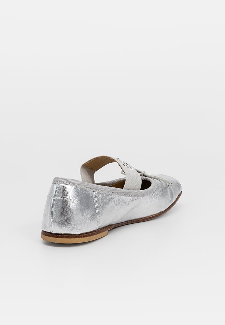 Scarpa piatta metallica argentata con punta rotonda, cinturino elastico e finitura texturizzata. Presenta una suola in gomma marrone e dettagli di cucitura discreti.