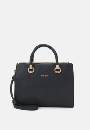 Sac à main noir texturé avec des poignées doubles, une section de poignée tressée, des accents en métal doré, et une bandoulière amovible. Détail du logo doré visible.