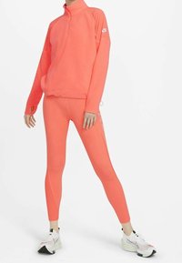 Sudadera atlética ligera en un brillante color coral, con media cremallera, manga larga y agujeros para los pulgares; combinada con leggings a juego que cuentan con rayas.