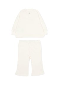 Dwuczęściowy strój w kolorze kremowym, składający się z bluzki z długim rękawem i zapięciem na zatrzaski z tyłu oraz dopasowanych spodni z elastycznym pasem.