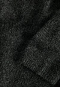 Tecido de suéter tricotado em cinza escuro com uma textura suave. Apresenta punhos canelados e um padrão consistente por toda a superfície.