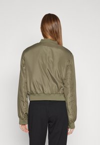 Broskně zelená bomber bunda s hladkým, lesklým povrchem, ribbovanými manžetami a pasem, se uvolněným střihem a minimalistickým designem.