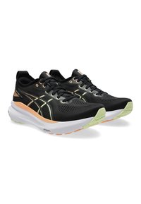 Zwarte sportschoenen met een bovenkant van mesh, contrasterende witte en groene zool en oranje accenten. Voorzien van een vetersluiting en een ademend ontwerp.