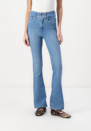 Modre visokotrgane flare jeans iz denima z gladko teksturo, z dvojnim gumbom in sprednjimi žepe. Poudarjene z balerinkami z leopardjim vzorcem.