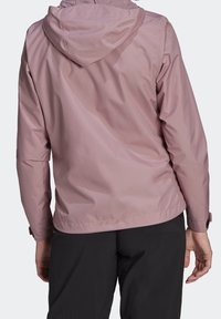 Světle růžová nepromokavá bunda s kapucí, hladká textura, elastické manžety a stahovací lem. Neobsahuje žádné viditelné loga ani vzory.