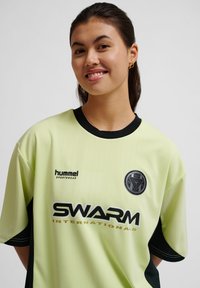 Limegrønt sportstrøje med sorte detaljer, der har korte ærmer, en rund hals og logoer for "hummel" og "SWARM International."