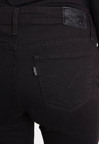 Svarta denimjeans med en slät textur, med en läderlapp med logotyp på baksidan och kontrasterande sömmar på bakfickorna.