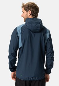 Marineblaue Windjacke mit hellblauen Akzenten, Kapuze und elastischen Bündchen. Hergestellt aus strukturierter, wasserabweisender Material mit einem Logo am Saum.