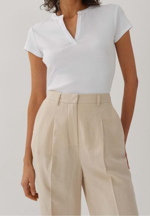 Top blanco de manga corta con textura acanalada y diseño de cuello en V, combinado con pantalones de talle alto en beige claro con pliegues.