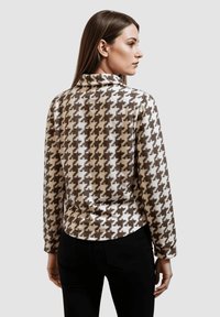 Top de patrón de espiga marrón y blanco con cuello simulado, silueta ajustada y mangas largas. Fabricado en una suave tela texturizada.