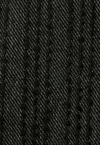 Musta herringbone-kuvioinen kangas hienovaraisella printillä. Materiaali näyttää olevan kudottu, esittäen hienoja pystysuoria ja diagonaalisia viivoja.