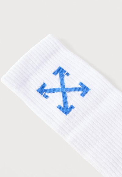 Tissu blanc côtelé avec une broderie bleue en forme de croix composée de quatre flèches pointant vers l'extérieur dans différentes directions.