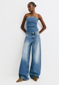 Top fără bretele din denim cu un design ajustat; blugi largi, de un albastru deschis, cu un spălătură în gradient și accente cu cuie pe părțile laterale.