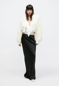 Casaco curto de pêlo branco sintético, usado por cima de uma blusa transparente com folhos, combinado com uma saia preta em cetim elegante, com detalhes pontiagudos brancos.