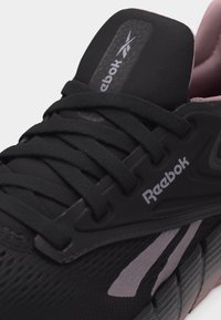 Κοντινό πλάνο μαύρου αθλητικού παπουτσιού Reebok με μαύρα κορδόνια, γκρι λωρίδες λογότυπου και λεπτομέρειες μαλακής σόλας.
