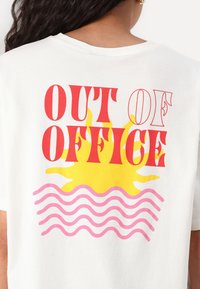Valge T-särk, millel on julge punane ja kollane tekst "OUT OF OFFICE" kollase päikesegraafiku kohal, allpool on roosa laineline joon.