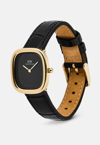 Montre Daniel Wellington avec un cadran carré noir, un boîtier doré, des aiguilles dorées et un bracelet en cuir noir avec une doublure intérieure beige et une boucle dorée.