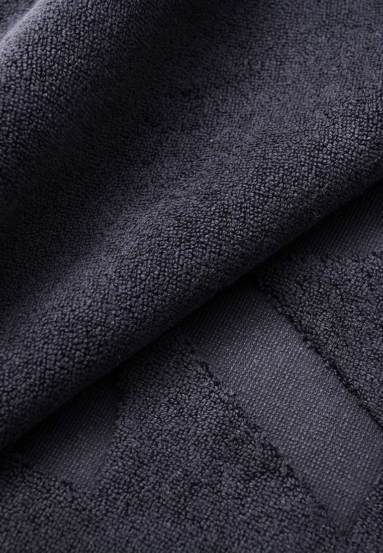 Ciemnoniebieska, teksturowana tkanina o miękkiej, puszystej powierzchni. Posiada gładki, tkany pasek oraz grubą, chłonną jakość.