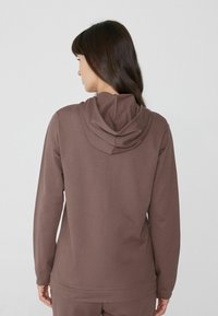 Sudadera marrón con capucha de doble capa, manga larga y un corte relajado. Hecha de una tela suave y texturizada con un dobladillo recto.