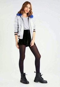 Casaco bomber prateado com gola de pêlo azul sintético, combinado com calções pretos de bombazina. Modelo usa meias opacas pretas e botas militares.