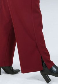 Burgundy wide-leg trousers with side slits. Paired with black heeled shoes featuring a textured, crocodile-like finish.