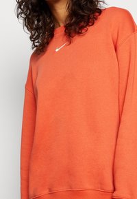 Orange sweatshirt i mjuk bomull, med rund hals och långa ärmar. Inkluderar en liten vit Nike-logotyp på bröstet.