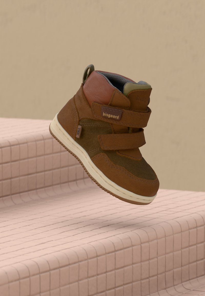 Zapato infantil marrón con dos correas de Velcro, materiales de ante y cuero, suela de goma y un lazo en el talón para facilitar su colocación.