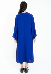 Langärmliges, blaues Kleid mit einem hohen Ausschnitt und Puffärmeln, das bis zur Mitte der Waden reicht. Reißverschluss im Rücken, glatte Textur, schlichtes Design.