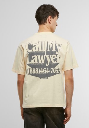 Beige bomulds t-shirt med et iøjnefaldende grafik på ryggen med "Ring til min advokat" og et telefonnummer, med en afslappet pasform og korte ærmer.