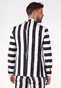 Čierno-biely pruhovaný sakó s rôznymi šírkami pruhov a textúrovaným povrchom. Obsahuje jeden rozventilovaný otvor a gombíkové manžety.