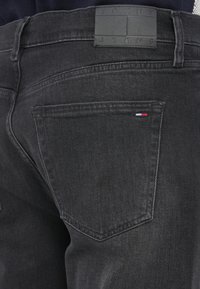 Fekete farmernadrág bőrből készült címkével, amelyen a "TOMMY JEANS" felirat található a deréknál. Két hátsó zseb és varrási részletek jellemzik.